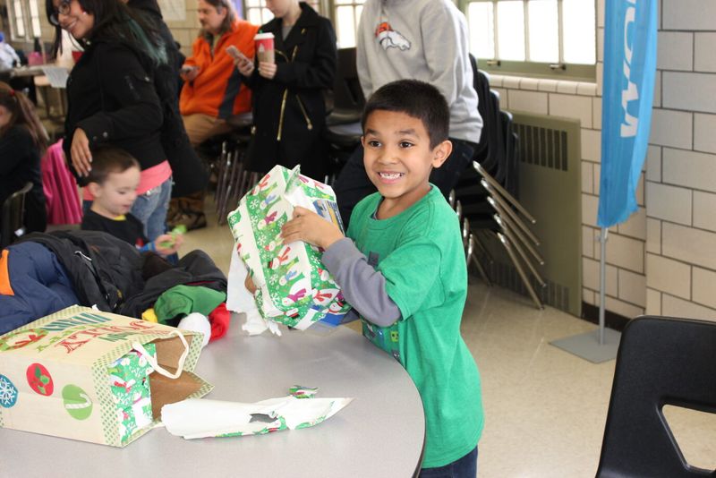 A boy grinning as he opens a wrapped holiday gift